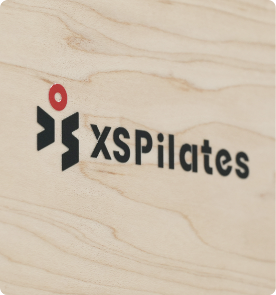 XSPilates brand logo on wood surface